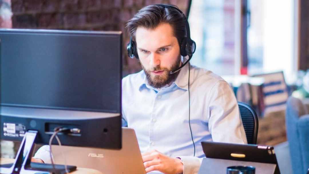 Man in business attire wearing a headset working on a computer in an office