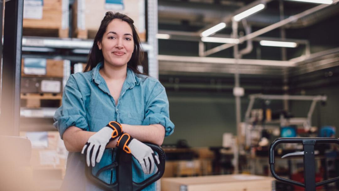 Woman warehouse worker wearing gloves posing at a pallet jack