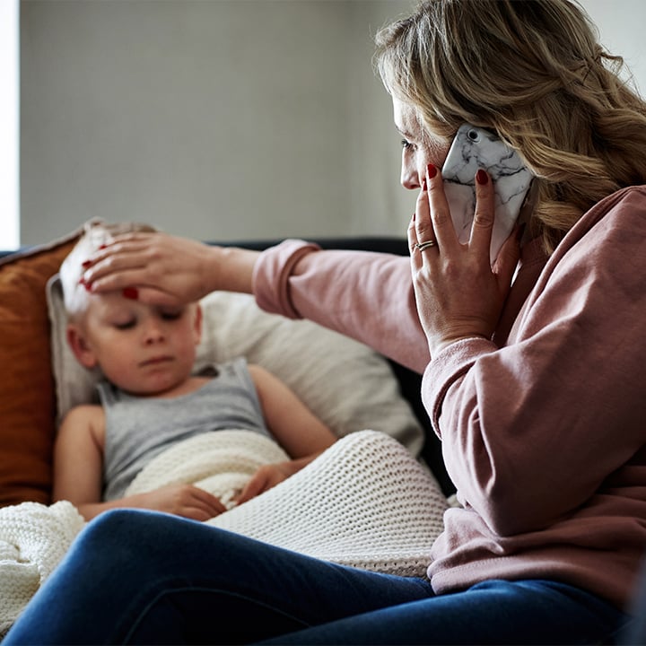 adult on the phone with their hand on a child's forehead