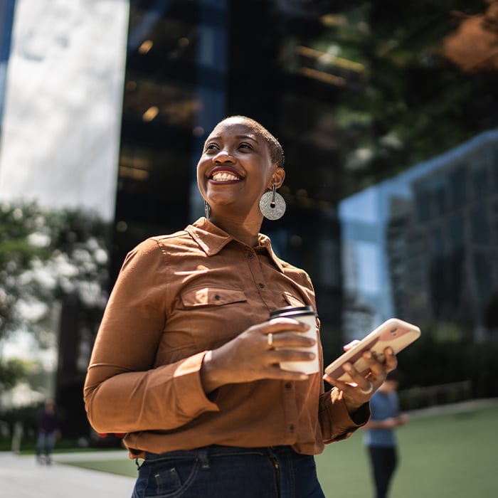 person happy walking outside holding their phone and cup 