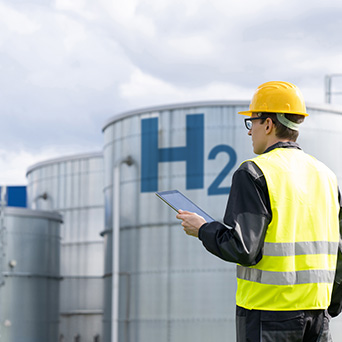 man with an orange construction hat and reflective vest holding a clipboard in front of metal containers 