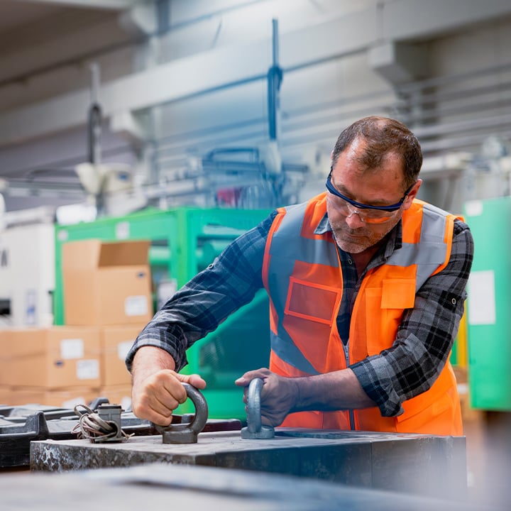 man wearing safety glasses and a reflective vest working with two pieces of metal loops