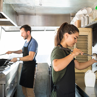 two people working on a food truck wearing aprons