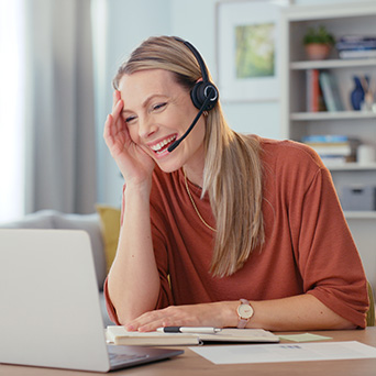 woman wearing a headset talking while looking at her laptop