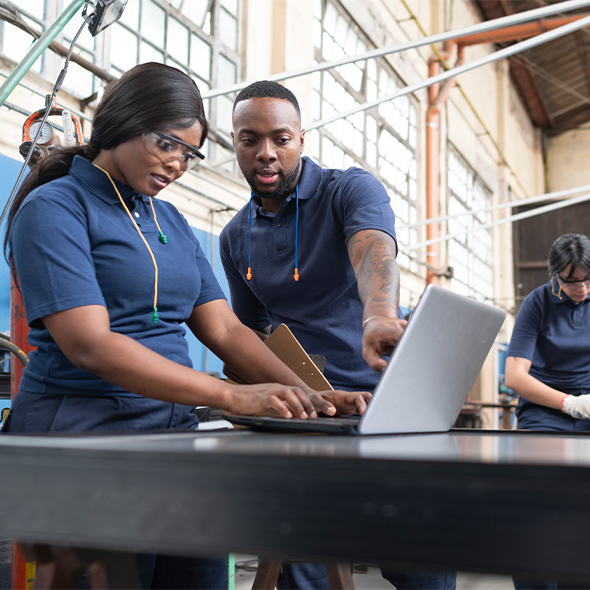 two workers look at laptop with ppe on