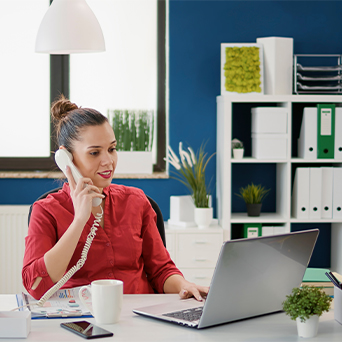 woman wearing red talking on a phone while looking at a laptop