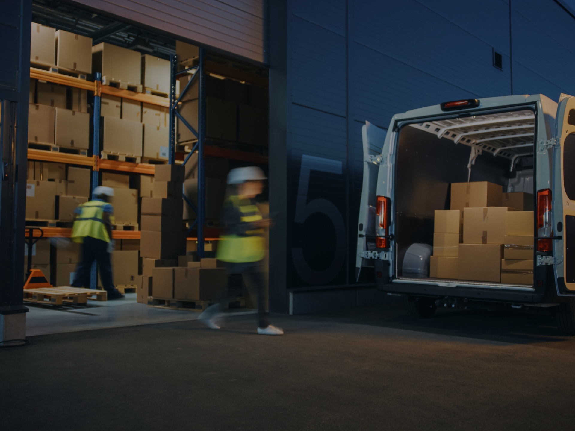 Warehouse workers in reflective vests loading a cargo van with boxes. 